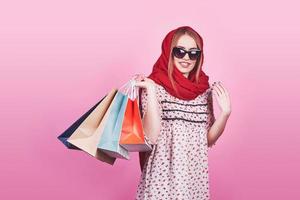 Porträt der jungen glücklichen lächelnden Frau mit Einkaufstüten auf dem rosa Hintergrund foto