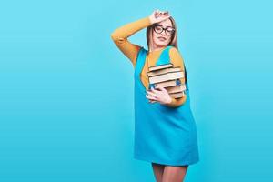Verwirrtes süßes Mädchen, das in den Händen einen Stapel Bücher hält, die auf buntem blauem Hintergrund isoliert sind foto