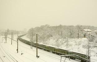 ein langer zug von güterwagen bewegt sich entlang der bahngleise. Eisenbahnlandschaft im Winter nach Schneefall foto