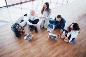 junge kreative leute im modernen büro. Gruppe junger Geschäftsleute arbeitet mit Laptop zusammen. Freiberufler sitzen auf dem Boden. Zusammenarbeit Unternehmenserfolg. Teamwork-Konzept