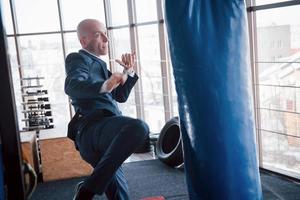 ein wütender kahlköpfiger geschäftsmann schlägt im fitnessstudio eine boxbirne. Konzept der Wutbewältigung foto