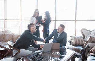 Willkommen an Bord von zwei gutaussehenden Männern, die sich im Büro mit ihren Kollegen die Hände schütteln. Junges Team von Mitarbeitern, die großartige Geschäftsgespräche im modernen Coworking-Büro führen. Teamwork-Menschen-Konzept foto