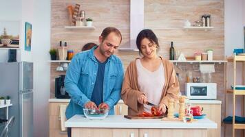 Ehefrau Hacken Glocke Pfeffer auf Schneiden Tafel und Mann öffnet Kühlschrank Tür. Kochen vorbereiten gesund organisch Essen glücklich zusammen Lebensstil. heiter Mahlzeit im Familie mit Gemüse foto