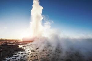 Strokkur-Geysir-Ausbruch in Island. fantastische Farben leuchten durch den Dampf. schöne rosa Wolken am blauen Himmel foto