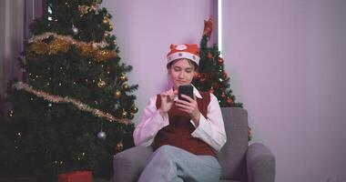 Porträt von jung Frau sitzen gemütlich Couch verwenden Zelle Telefon im Haus mit Weihnachten Ornament, feiern Weihnachten und Neu Jahr foto