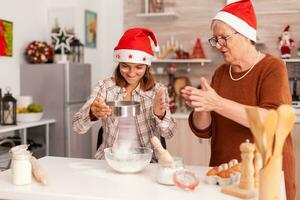 glücklich Enkel vorbereiten hausgemacht Teig putten Mehl im Schüssel mit Sieb Kochen traditionell Lebkuchen Dessert mit Oma feiern Weihnachten Urlaub. Kind genießen Winter Jahreszeit foto
