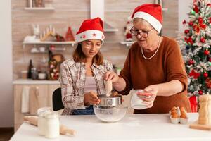 heiter Kind Herstellung traditionell Teig putten Mehl im Schüssel mit Sieb Kochen hausgemacht Lebkuchen Dessert mit Oma feiern Weihnachten Jahreszeit. Kind genießen Winter Urlaub foto