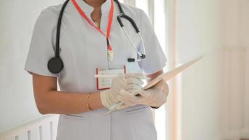 Ausgeschnittene Aufnahme einer Krankenschwester, die Handschuhe mit einem Tablet trägt, um eine mit dem Covid-19-Virus infizierte Person aufzuzeichnen.