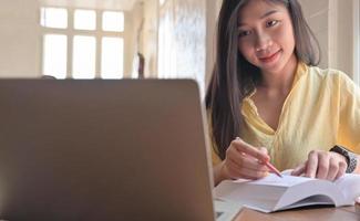 Asiatische Studentin im Teenageralter sucht nach Informationen vom Laptop und macht sich Notizen. Sie bereitet sich auf die Aufnahmeprüfung für die Universität vor.
