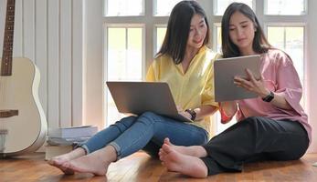 Zwei asiatische Frauen benutzen während des Ausbruchs des Virus Laptop in ihrer Freizeit zu Hause. foto