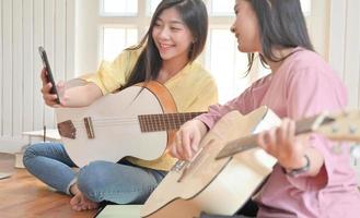 Mädchen und Freunde im Teenageralter, die Gitarre spielen und einen Smartphone-Videoanruf verwenden.