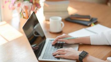 Nahaufnahme, die Hand des jungen Mädchens benutzt einen Laptop auf einem Holzschreibtisch im Büro mit schöner Beleuchtung. foto