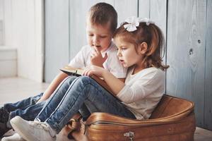 bereit für große Reisen. glückliches kleines Mädchen und Junge, die ein interessantes Buch lesen, das eine große Aktentasche trägt und lächelt. Reise-, Freiheits- und Vorstellungskonzept