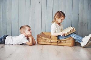bereit für große Reisen. glückliches kleines Mädchen und Junge, die ein interessantes Buch lesen, das eine große Aktentasche trägt und lächelt. Reise-, Freiheits- und Vorstellungskonzept