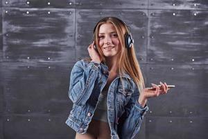 Mode, Kleidung, Menschenkonzept. attraktive sexy junge Frau mit Jeansjacke. Mädchen posiert im Studio hört Musik über Kopfhörer foto