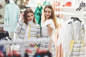 toller Tag zum Einkaufen. Zwei schöne Frauen mit Einkaufstüten, die sich beim Gehen im Bekleidungsgeschäft mit einem Lächeln ansehen foto