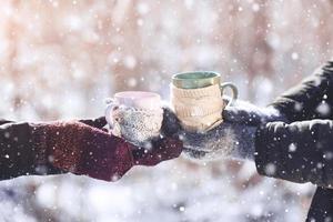 paar hände in handschuhen nehmen eine tasse mit heißem tee im winterpark foto