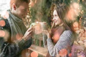 Foto von glücklichem Mann und hübscher Frau mit Tassen im Freien im Winter. Winterurlaub und Urlaub. Weihnachtspaare des glücklichen Mannes und der Frau trinken heißen Wein. verliebtes Pärchen