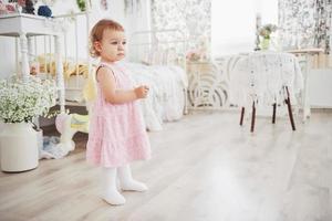 schönes kleines Mädchen, das Spielzeug spielt. blauäugige Blondine. weißer Stuhl. Kinderzimmer. glückliches kleines Mädchenporträt. Kindheit Konzept foto