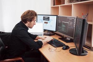 Männlicher Programmierer, der an einem Desktop-Computer mit vielen Monitoren im Büro in einer Softwareentwicklungsfirma arbeitet. Website-Design-Programmierung und Codierungstechnologien foto