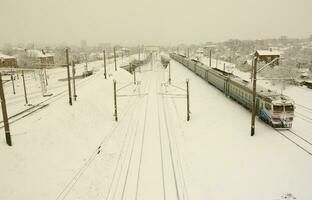 Ein langer Zug von Personenwagen bewegt sich entlang der Bahnstrecke. Eisenbahnlandschaft im Winter nach Schneefall foto