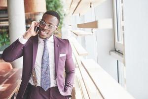 Porträt eines jungen und gutaussehenden afroamerikanischen Geschäftsmannes, der in einem Anzug am Telefon spricht