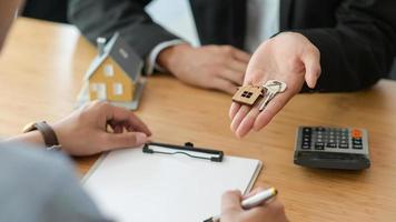 Ausschnitt der Unterzeichnung eines Hauskaufvertrags, während der Makler den Hausschlüssel hält.