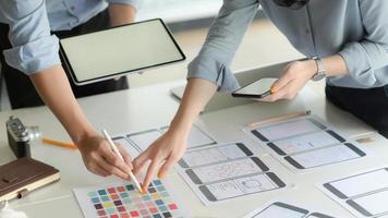Zugeschnittene Aufnahme eines jungen UX-Designerteams, das an einem Smartphone-Anwendungsprojekt mit digitalem Tablet in einem modernen Büroraum arbeitet.