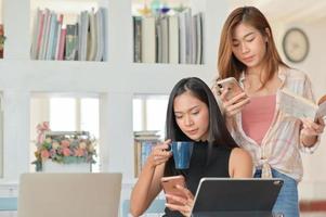 Zwei asiatische Studentinnen halten eine Kaffeetasse und schauen auf ein Smartphone, um sich auf das Studium vorzubereiten. foto