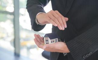 Versicherungsagent hält ein Hausmodell in der Hand, das das Symbol der Hausratversicherung zeigt.