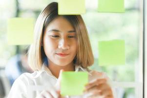 asiatische Frau plant und schreibt Notizen auf Papier auf Glas. foto