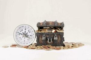 ein Truhe mit Münzen und ein Kompass auf ein Weiß Hintergrund foto