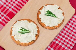 knusprig Cracker Sandwich mit Sahne Käse und Rosmarin auf hölzern Kochen Tafel auf Magenta Hintergrund foto