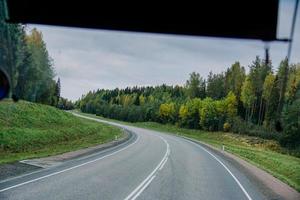 Blick auf die Straße und den herbstlichen Wald durch das Busfenster. Ausflug foto