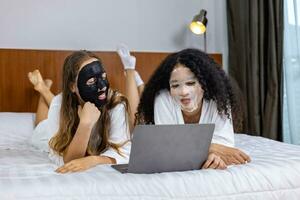 Paar von Freundin im Bademantel mit Gesichts- Maske auf Spa Nacht zum Schönheit Haut und Behandlung während Aufpassen Film zusammen im Bett zum Schlaf Über Datum Nacht und lgbtq homosexuell Lesben Konzept foto