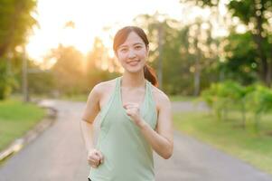 passen asiatisch jung Frau Joggen im Park lächelnd glücklich Laufen und genießen ein gesund draussen Lebensstil. weiblich Jogger. Fitness Läufer Mädchen im Öffentlichkeit Park. gesund Lebensstil und Wellness Sein Konzept foto