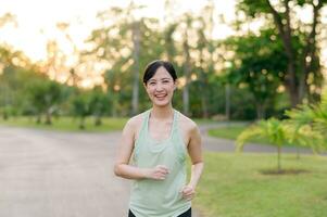 passen asiatisch jung Frau Joggen im Park lächelnd glücklich Laufen und genießen ein gesund draussen Lebensstil. weiblich Jogger. Fitness Läufer Mädchen im Öffentlichkeit Park. gesund Lebensstil und Wellness Sein Konzept foto