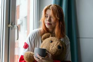 gemütlich Moment von Generation z rothaarig Teenager Mädchen mit heiß trinken und Teddy Bär foto