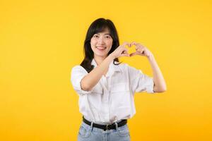 jung weiblich Gesundheitspflege. asiatisch Frau tragen Weiß Hemd fühlt sich glücklich und romantisch Formen Herz Geste drückt aus zärtlich Gefühl posiert isoliert auf Gelb Hintergrund. Menschen Zuneigung und Pflege Konzept. foto