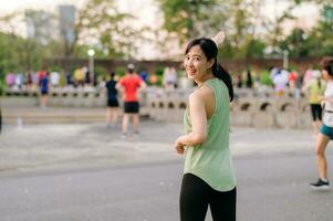 weiblich Jogger. passen jung asiatisch Frau mit Grün Sportbekleidung Aerobic tanzen Übung im Park und genießen ein gesund draussen. Fitness Läufer Mädchen im Öffentlichkeit Park. Wellness Sein Konzept foto