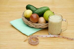 Glas von Smoothie gemischt Früchte, Korb von frisch Früchte und Messung Band. Konzept, gesund Getränk zum Gesundheit. Gut Sein und Gewicht Verlust Speisekarte. hausgemacht erfrischend Obst Getränke. hoch Fasern, Entgiftung. foto