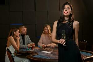 elegant dunkelhaarig Mädchen mit Glas von Champagner Stehen in der Nähe von Spielen Tabelle im Kasino foto
