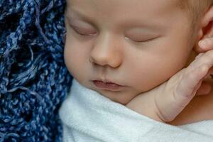 Neugeborene - - Baby, Gesicht Nahansicht. das Schlafen Neugeborene Junge unter ein Weiß gestrickt Decke Lügen auf das Blau Fell. foto