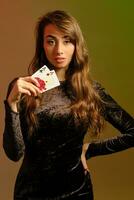 Brünette Frau im schwarz Kleid zeigen zwei rot Chips und Asse, posieren gegen bunt Studio Hintergrund. Glücksspiel, Poker, Kasino. Nahansicht. foto