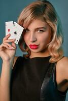 blond Mädchen im schwarz stilvoll Kleid zeigen zwei spielen Karten, posieren gegen Blau Hintergrund. Glücksspiel Unterhaltung, Poker, Kasino. Nahansicht. foto