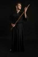 Kendo Guru tragen im ein traditionell japanisch Kimono ist üben kriegerisch Kunst mit das shinai Bambus Schwert gegen ein schwarz Studio Hintergrund. foto