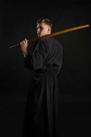 Kendo Guru tragen im ein traditionell japanisch Kimono ist üben kriegerisch Kunst mit das shinai Bambus Schwert gegen ein schwarz Studio Hintergrund. foto