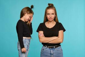 Mama und Tochter mit ein komisch Frisuren, gekleidet im schwarz Hemden und Blau Denim Jeans sind posieren gegen ein Blau Studio Hintergrund. Nahansicht Schuss. foto