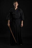 Kendo Guru tragen im ein traditionell japanisch Kimono ist üben kriegerisch Kunst mit das shinai Bambus Schwert gegen ein schwarz Studio Hintergrund. foto