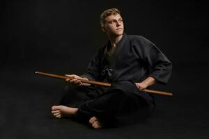 Kendo Guru tragen im ein traditionell japanisch Kimono ist üben kriegerisch Kunst mit das shinai Bambus Schwert gegen ein schwarz Studio Hintergrund. foto